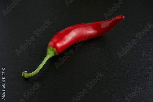 Isolated red hot chili pepper on black stone background, ideal ingredient for spicy and passionate recipes