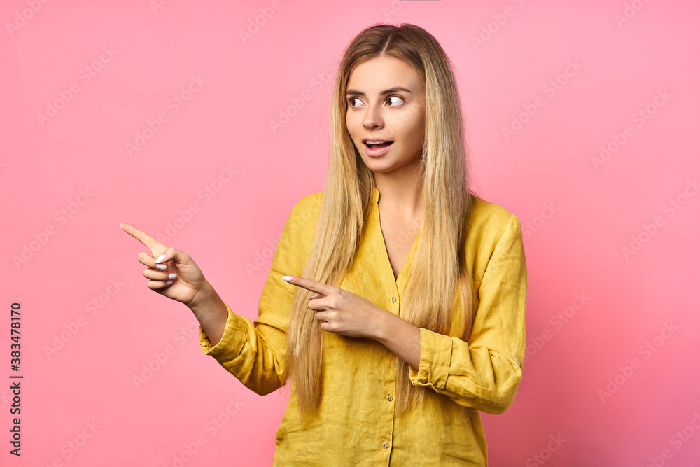 Portrait of a young blonde positive woman with a cheerful facial expression rejoices. shows a finger to the side, isolated on a pink background. Beautiful woman indoors. Portrait of a young blonde positive woman with a cheerful facial expression rejoices. shows a finger to the side, isolated on a pink background. Beautiful woman indoors.