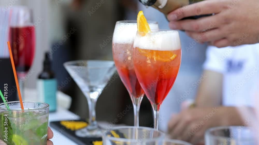 Close up, the bartender pours champagne into glasses with orange slices, and foam forms. The waiter prepares drinks for the guests.