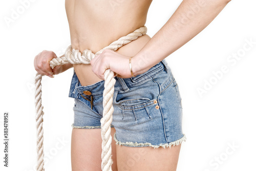 Woman's waist in ropes in short denim shorts on a white background. Bondage