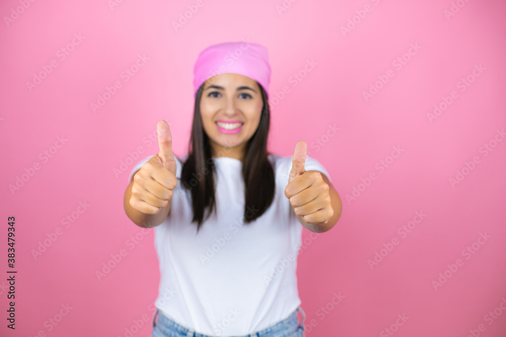 Young beautiful woman wearing pink headscarf over isolated pink background smiling and doing the ok signal with her thumbs Young beautiful woman wearing pink headscarf over isolated pink background smiling and doing the ok signal with her thumbs