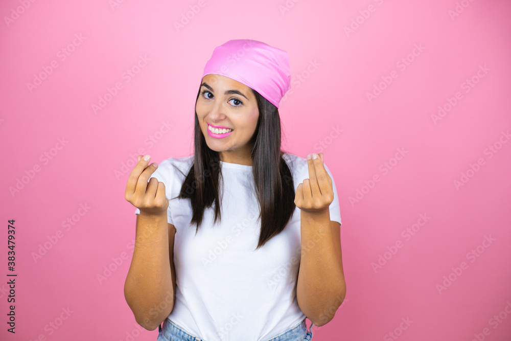 Young beautiful woman wearing pink headscarf over isolated pink background doing money gesture with hands, asking for salary payment, millionaire business Young beautiful woman wearing pink headscarf over isolated pink background doing money gesture with hands, asking for salary payment, millionaire business