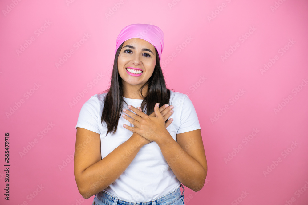Young beautiful woman wearing pink headscarf over isolated pink background smiling with her hands on her chest and grateful gesture on her face. Young beautiful woman wearing pink headscarf over isolated pink background smiling with her hands on her chest and grateful gesture on her face.
