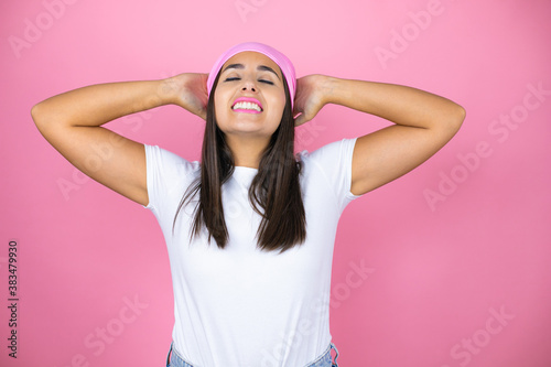 Young beautiful woman wearing pink headscarf over isolated pink background relaxing and stretching, arms and hands behind head and neck smiling happy