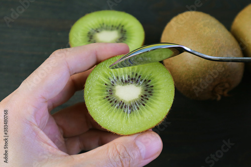 Closeup Hand Holding Cut Kiwifruit Scooping with a Spoon on Black Background photo