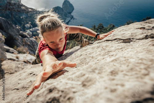 Brave young woman climber fearlessly climbs up sheer stone wall in mountains, overcoming obstacles. Dangerous chasm balancing, adrenaline and courage in extreme sports photo