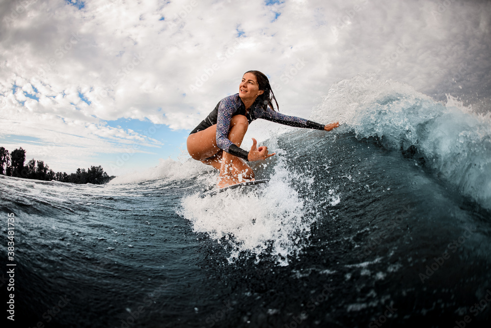 woman riding on wave sitting on surf board and touching the water with her hand.