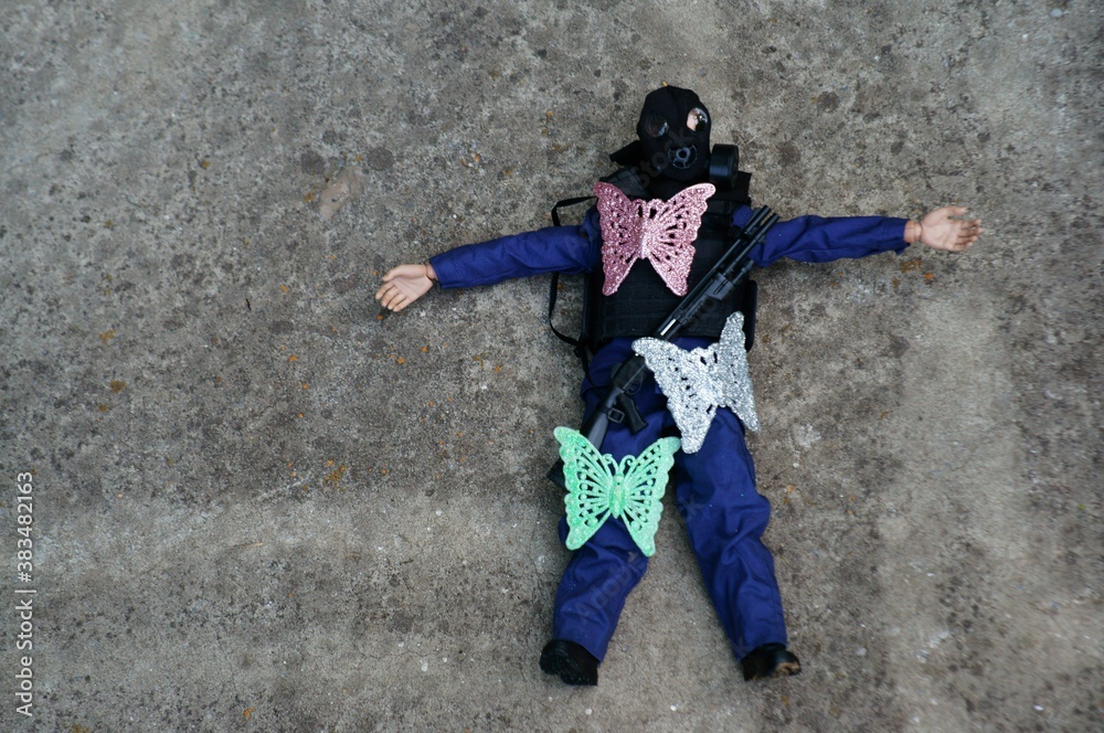Fototapeta premium A toy soldier with a gas mask and a rifle on a concrete slab. There are several toy butterflies on the figure.
