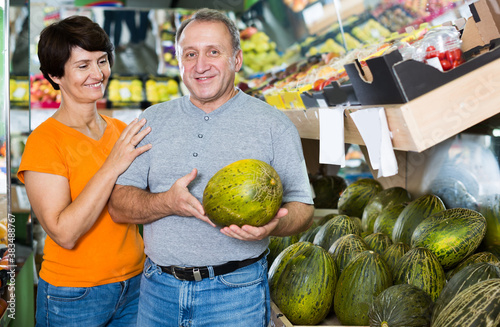 Smiling man and his wife are choosing ripe melon in the fruit store