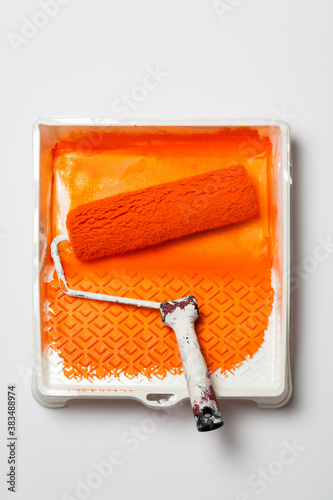 Orange paint roller in tray with orange paint on white background