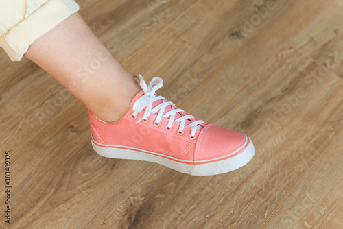 Casual pink shoes sneakers on woman feet on wooden floor background