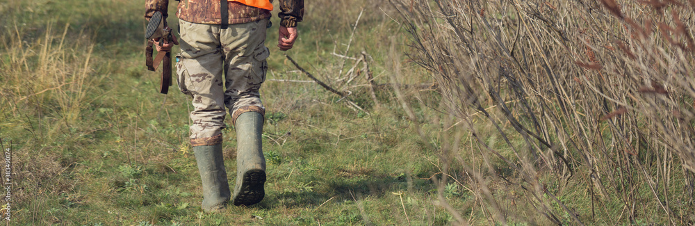 Duck hunter with shotgun walking through a meadow.