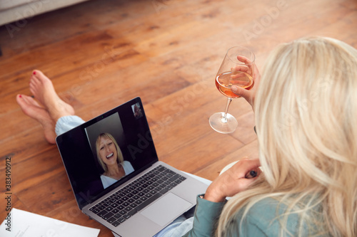 Woman Having Video Chat With Friend Sitting On Floor At Home Relaxing With Wine