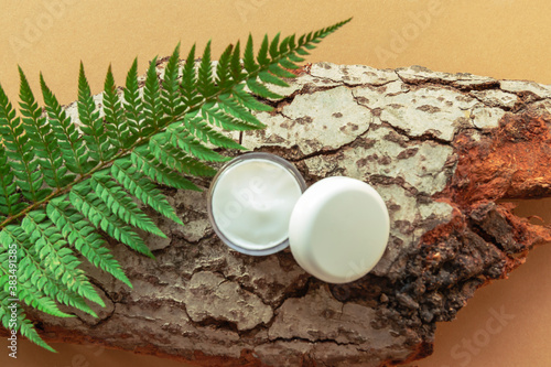 White jar with cream on the bark of a tree, fern leaves. Natural cosmetics concept. Yellow background