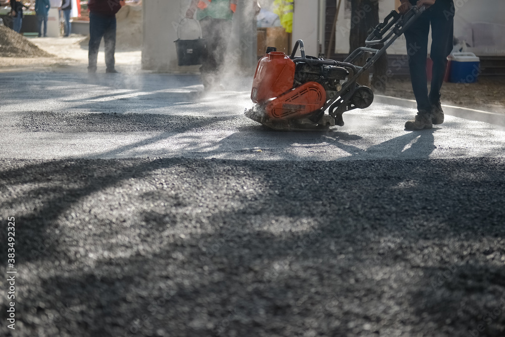 Obraz premium Asphalt paving with manual motorized roller. Steam coming out from asphalt.