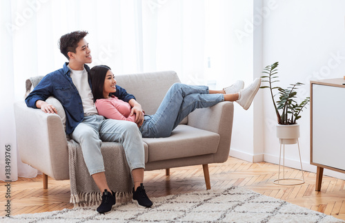 Asian Couple Relaxing Sitting On Sofa At Home Enjoying Weekend