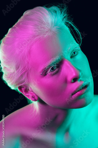 Alien. Close up portrait of beautiful albino girl on dark background in neon light. Blonde female model with dreamlike make-up and well-kept skin. Concept of beauty, cosmetics, style, fashion.