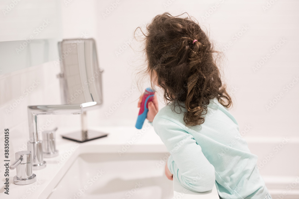 Young girl child toddler brushing her teeth in the bathroom at the basin with a large mirror modern white clean simple bathroom Young girl child toddler brushing her teeth in the bathroom at the basin with a large mirror modern white clean simple bathroom