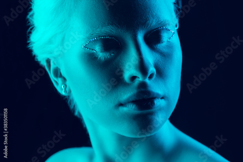Night. Close up portrait of beautiful albino girl on dark background in neon light. Blonde female model with dreamlike make-up and well-kept skin. Concept of beauty, cosmetics, style, fashion.