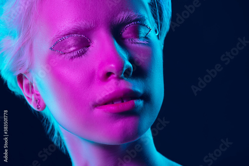 Sleepy. Close up portrait of beautiful albino girl on dark background in neon light. Blonde female model with dreamlike make-up and well-kept skin. Concept of beauty, cosmetics, style, fashion.