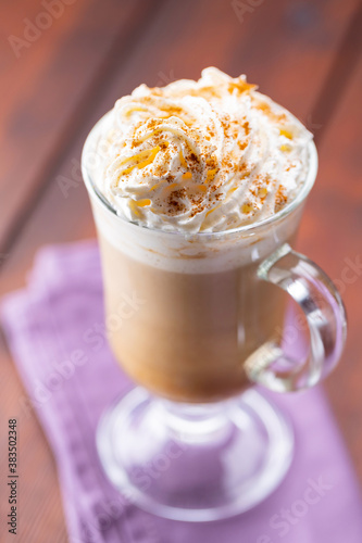 Pumpkin spice latte in a glass mug. Pumpkin latte with whipped cream and spices on a wooden boards. Hot autumn coffee drink on a linen napkin