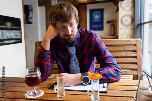 Sad young man sits alone in a bar. Unhealthy lifestyle, alcohol addiction, crisis, unemployment, dismissal.