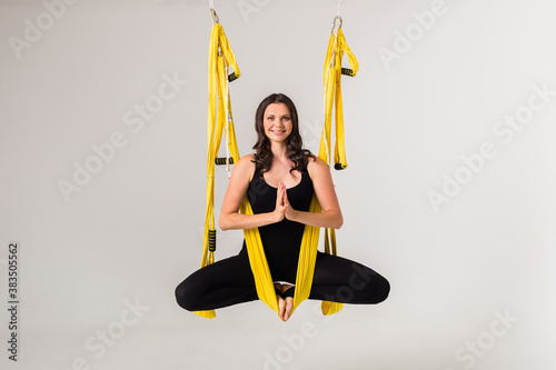 a young female sportswoman is engaged aeroyoga in a yellow hammock on a white isolated background. Namaste Pose photo