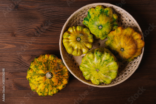 Colorful pattypan squash in wicker plate on wooden background. Top view.
