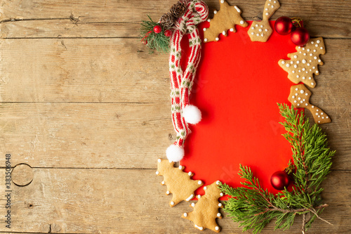 frame for Christmas greetings made of gingerbread cookies, fir twigs, red Christmas decorations. red frame background an a light brown wooden background photo