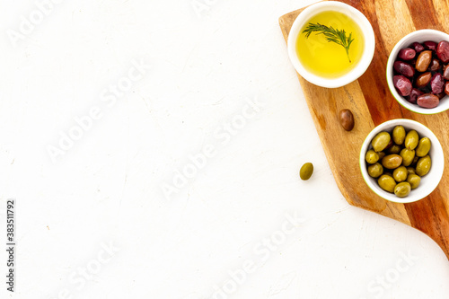 Green and black olives, olive oil in bowls on cutting board top-down copy space