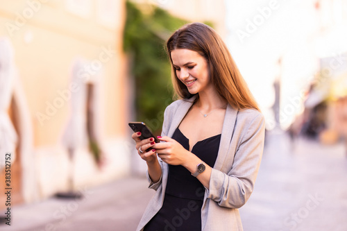 Smiling woman walks down the central city street and uses her phone. Pretty summer woman walks down the street looking at her mobile phone