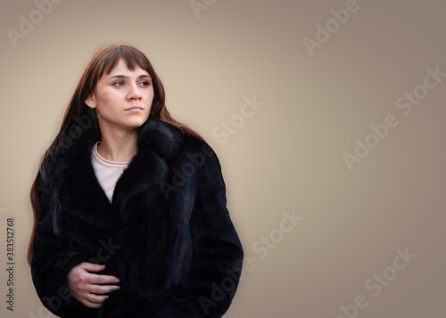 Girl in a black fur coat on a light gray background. Young woman in a mink fur coat on an isolated light background. Beauty and fashion concept. © Ekaterina