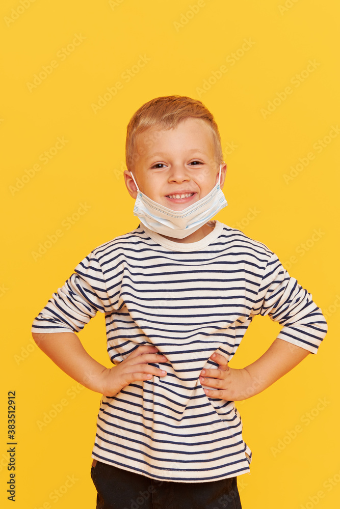 Portrait of cute little child boy wearing protective mask on yellow background. Virus protection and healthcare concept during COVID pandemic