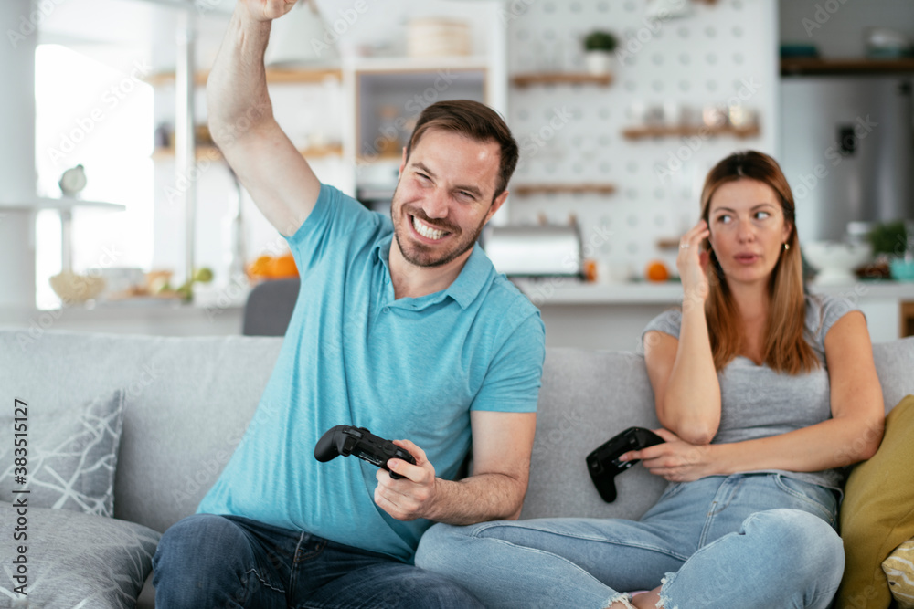 Husband and wife playing video game with joysticks in living room. Loving couple are playing video games at home. Husband and wife playing video game with joysticks in living room. Loving couple are playing video games at home.
