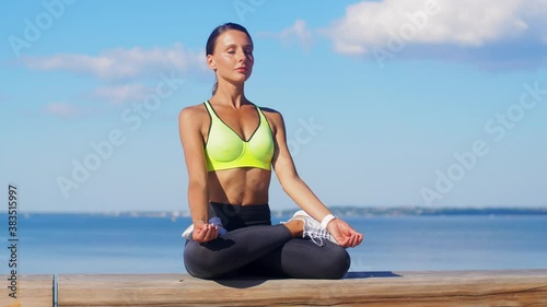 fitness, sport and yoga concept - young woman meditating in lotus pose at seaside photo