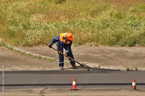 Laying asphalt by workers. Road construction. Modern technology of laying a highway with a solid surface. People work at a construction site. The worker is leveling the surface manually