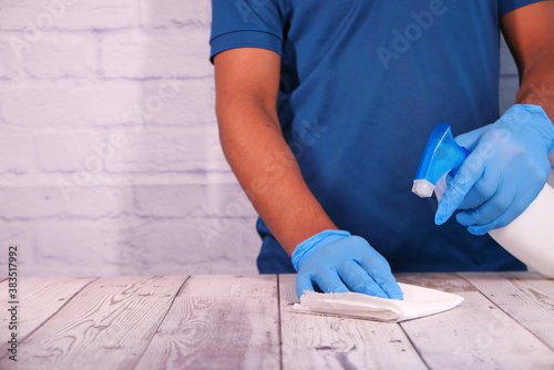 Person hand in disposable gloves using disinfectant spray to clean table surface