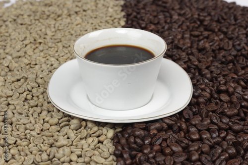 Black coffee is served in a glass cup, which is placed on top of the coffee beans. There are coffee beans that have been roasted and are still fresh beans.