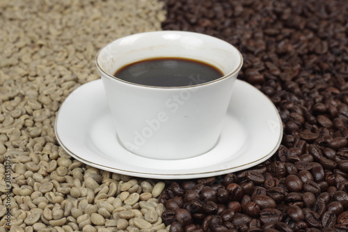 Black coffee is served in a glass cup, which is placed on top of the coffee beans which are arranged neatly to form a heart.
