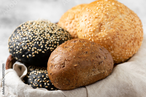 Sesame buns for burgers. Wheat and rye buns in a basket on a light gray background. Homemade buns with sesame seeds. Baking close-up