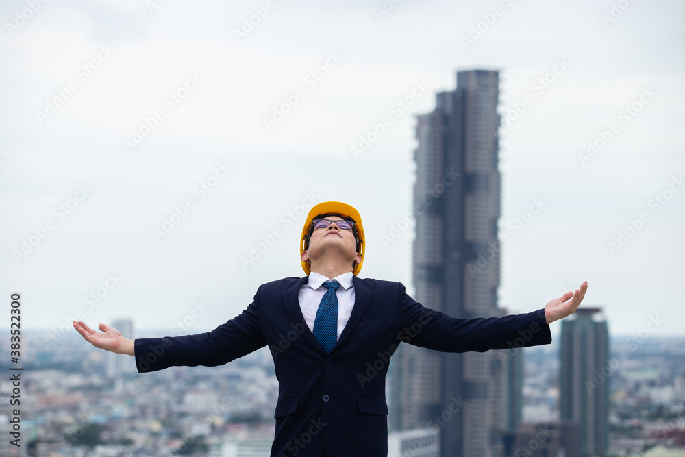architect man wear black suit and yellow helmet standing on building cityscape. looking for future concept.