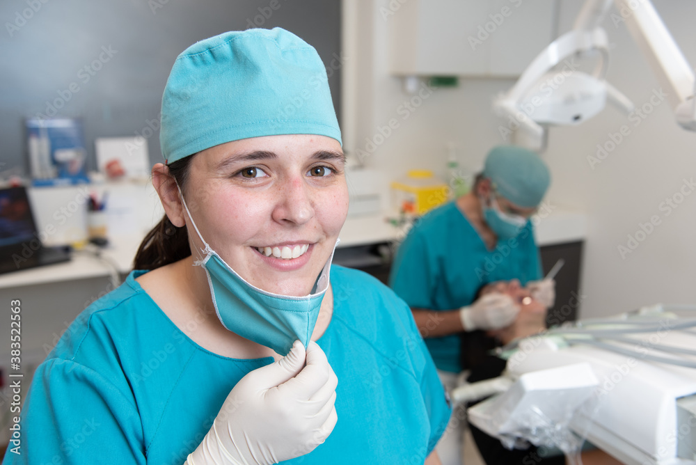 Portrait of an assistant nurse in a dental clinic office with the dentist working behind. Portrait of an assistant nurse in a dental clinic office with the dentist working behind.
