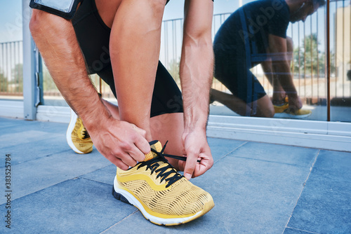 Sportsman tying his shoelaces. He is wearing yellow sneakers.