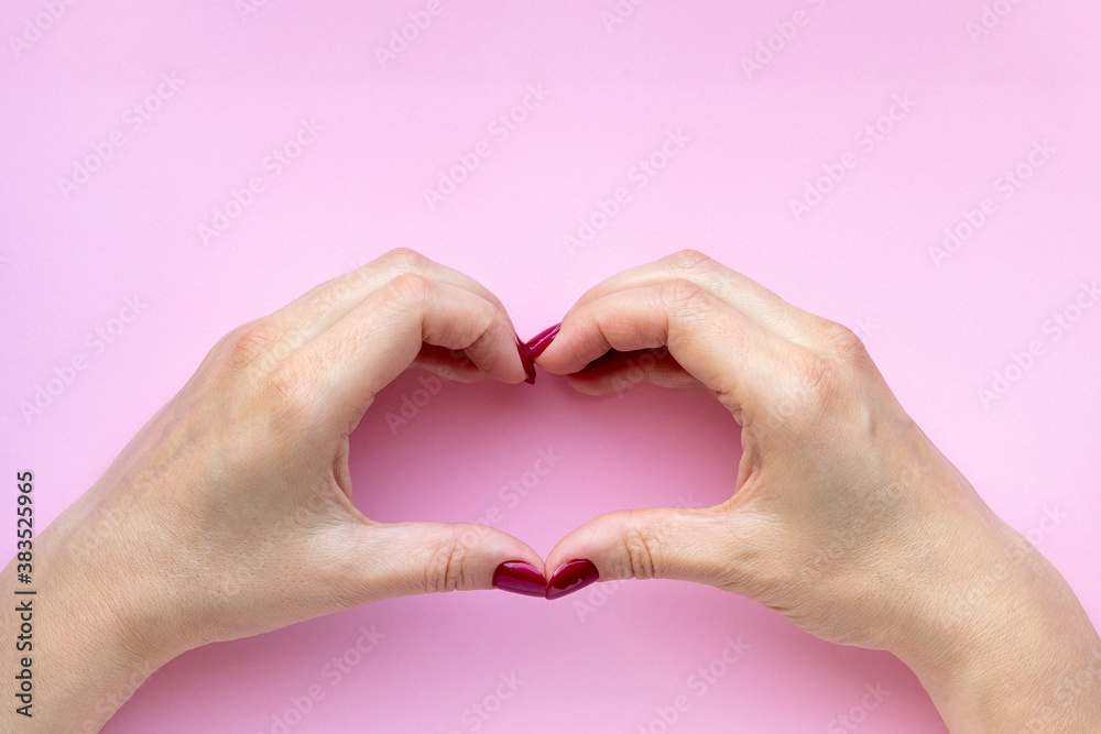 Woman's hands with beautiful glossy manicure - burgundy, dark red color nails making heart symbol on pink background Woman's hands with beautiful glossy manicure - burgundy, dark red color nails making heart symbol on pink background