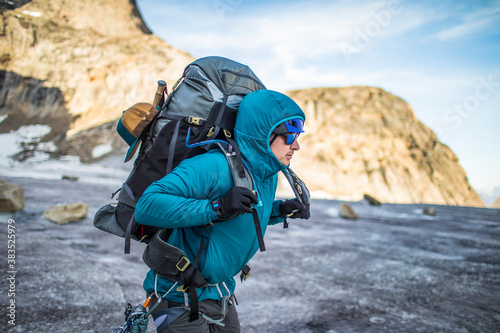 Mountaineer lifts heavy backpack onto shoulders while crossing glacier photo