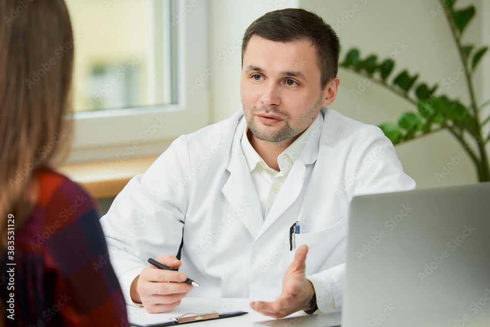A caucasian doctor in a white lab coat is sitting at a desk and describing the treatment to a female patient in a doctor's office. A woman with long hair at an appointment in a hospital. A caucasian doctor in a white lab coat is sitting at a desk and describing the treatment to a female patient in a doctor's office. A woman with long hair at an appointment in a hospital.