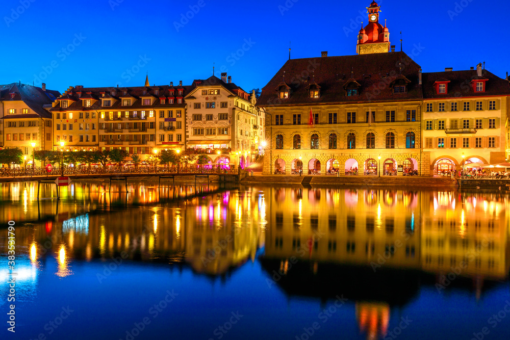 Medieval city of Lucerne on shores of Lake Lucerne, Vierwaldstatersee, illuminated by night. Kornschutte or town hall and buildings reflect in calm waters of Reuss river, Canton Lucerne, Switzerland.