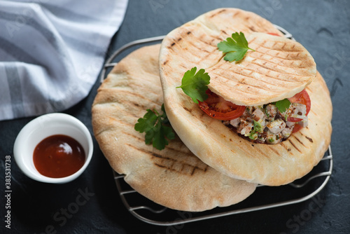 Grilled pitas stuffed with doner meat and vegetables on a metal cooling rack, horizontal shot on a black stone background