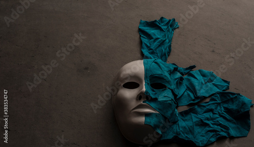White theater mask on a black background covered with leather flaps. Psychic symbol of overlapping layers.