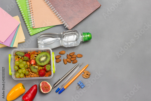 Lunchbox with nuts and fruits. Pens and notebooks, note paper. Bottle of water.
